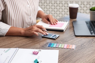 Photo of Woman writing in business planner and using calculator at wooden table in office, closeup