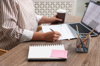 Photo of Woman using business planner at wooden table in office, closeup