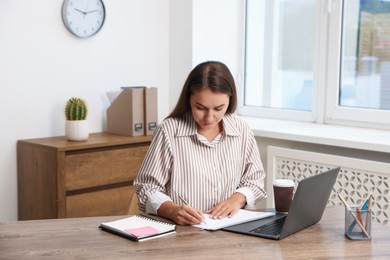 Photo of Woman using business planner at wooden table in office
