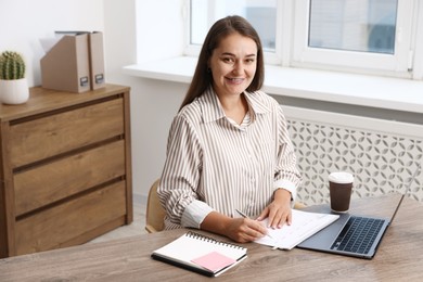 Photo of Woman using business planner at wooden table in office