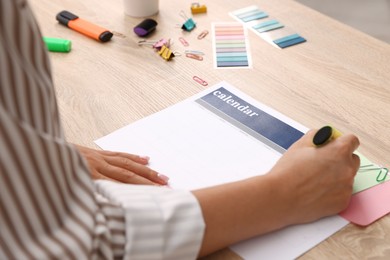 Photo of Business planning. Woman using calendar at wooden table in office, closeup