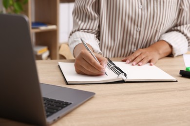 Photo of Woman using business planner at wooden table in office, closeup