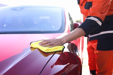 Photo of Man wiping car hood with yellow microfiber rag outdoors, closeup