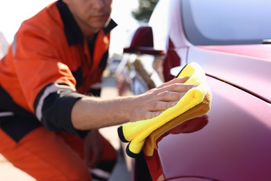 Photo of Man wiping car hood with yellow microfiber rag outdoors, closeup