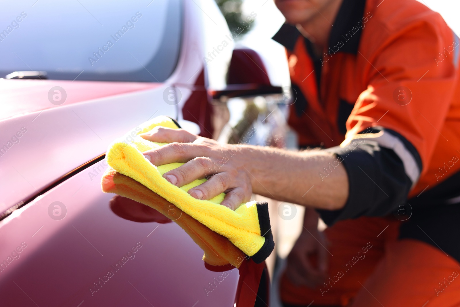 Photo of Man wiping car hood with yellow microfiber rag outdoors, closeup
