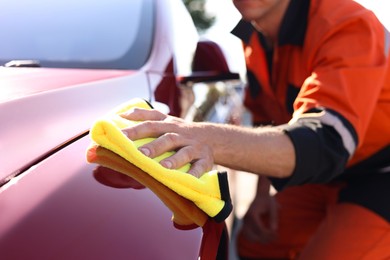 Photo of Man wiping car hood with yellow microfiber rag outdoors, closeup