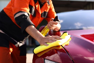 Photo of Man wiping car hood with yellow microfiber rag outdoors, closeup