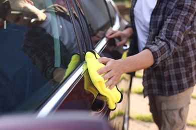 Photo of Man wiping car with yellow microfiber rag outdoors, closeup