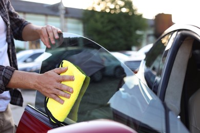 Photo of Man wiping car side window with yellow microfiber rag outdoors, closeup