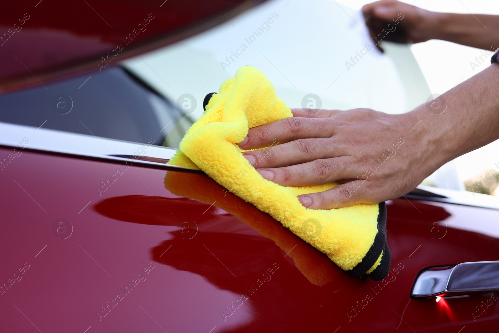 Photo of Man wiping car door with yellow microfiber rag outdoors, closeup