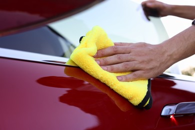 Photo of Man wiping car door with yellow microfiber rag outdoors, closeup