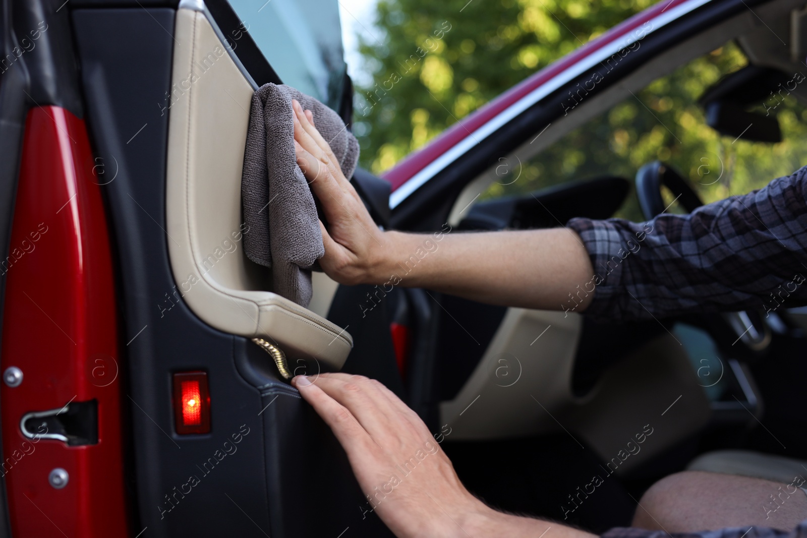 Photo of Man wiping open car door with grey microfiber rag outdoors, closeup