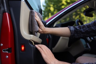 Photo of Man wiping open car door with grey microfiber rag outdoors, closeup