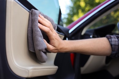 Photo of Man wiping open car door with grey microfiber rag outdoors, closeup