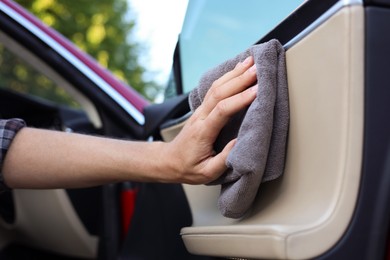 Photo of Man wiping open car door with grey microfiber rag outdoors, closeup