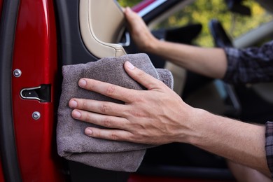 Photo of Man wiping open car door with grey microfiber rag outdoors, closeup