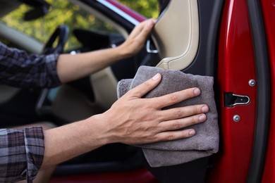 Photo of Man wiping open car door with grey microfiber rag outdoors, closeup