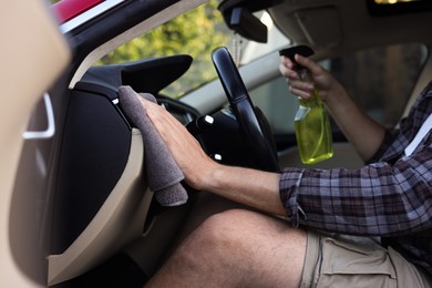 Photo of Man wiping car interior with grey microfiber rag in salon, closeup