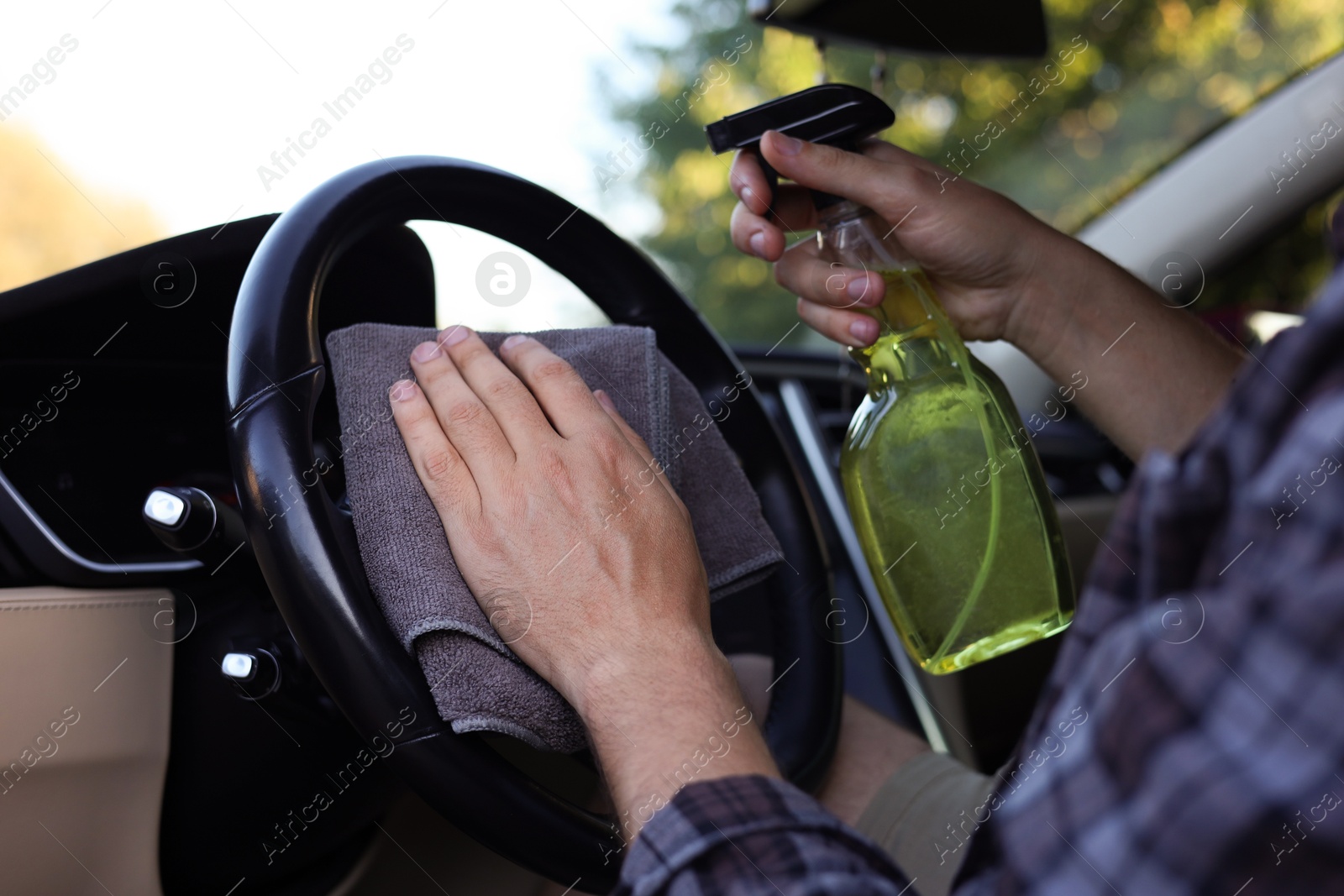 Photo of Man wiping steering wheel with grey microfiber rag in car salon, closeup