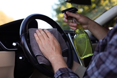Photo of Man wiping steering wheel with grey microfiber rag in car salon, closeup