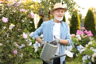 Photo of Elderly man in hat watering beautiful flowers with can in garden