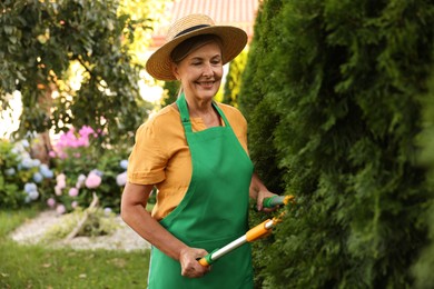 Photo of Senior woman in hat and apron with manual hedge trimmer working in garden