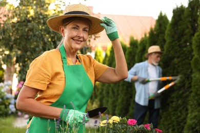 Photo of Senior couple in hats working with plants in garden, selective focus