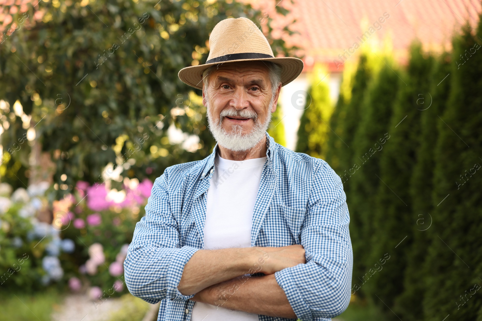Photo of Portrait of elderly man in hat with crossed arms in garden