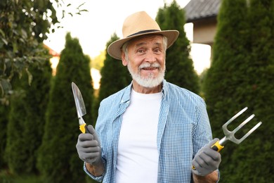 Photo of Portrait of smiling elderly man in hat with gardening tools outdoors