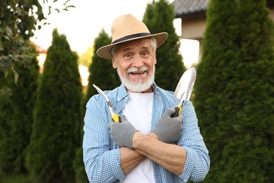 Photo of Portrait of smiling elderly man in hat with gardening tools outdoors