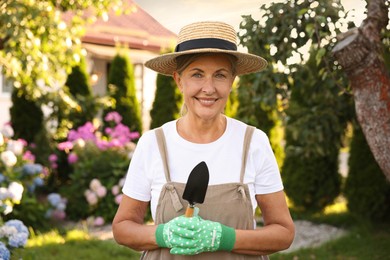 Photo of Portrait of smiling senior woman in hat, gloves and apron with shovel in garden