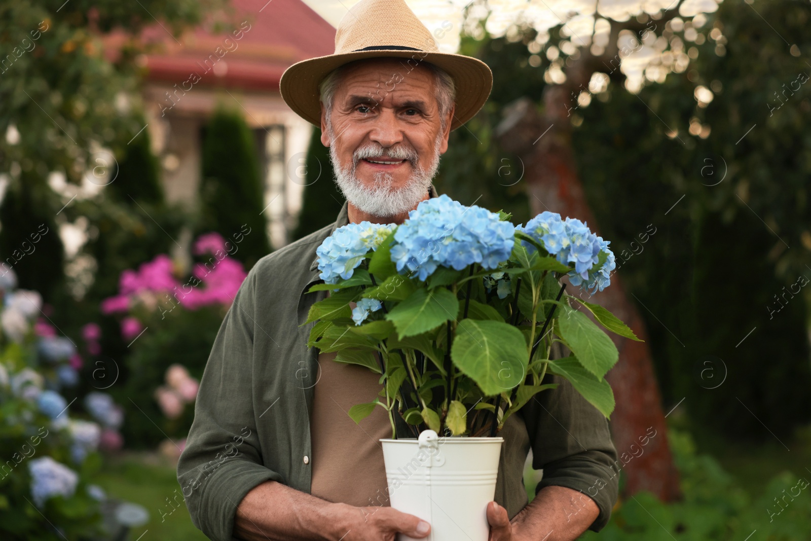 Photo of Portrait of smiling elderly man in hat with potted flowers in garden