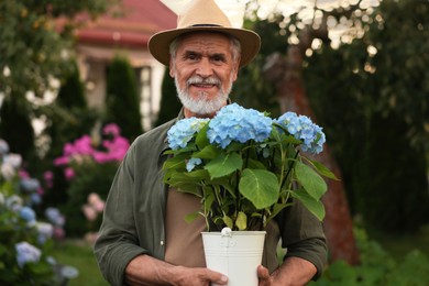Photo of Portrait of smiling elderly man in hat with potted flowers in garden