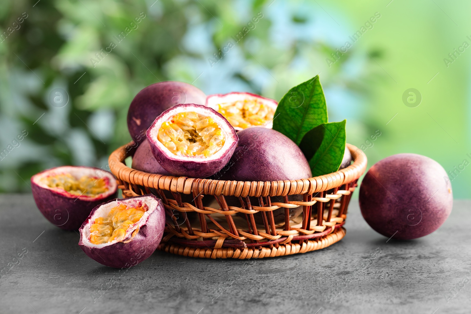 Photo of Fresh passion fruits in wicker basket on grey table outdoors, closeup