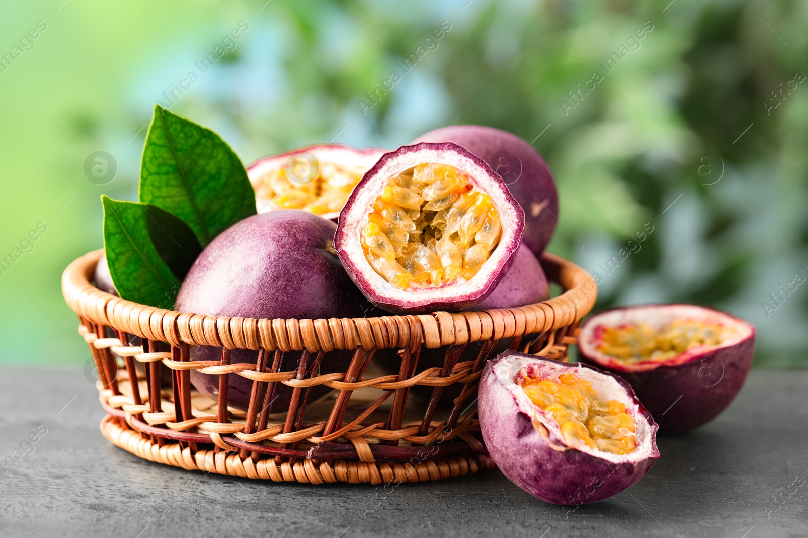 Photo of Fresh passion fruits in wicker basket on grey table outdoors, closeup