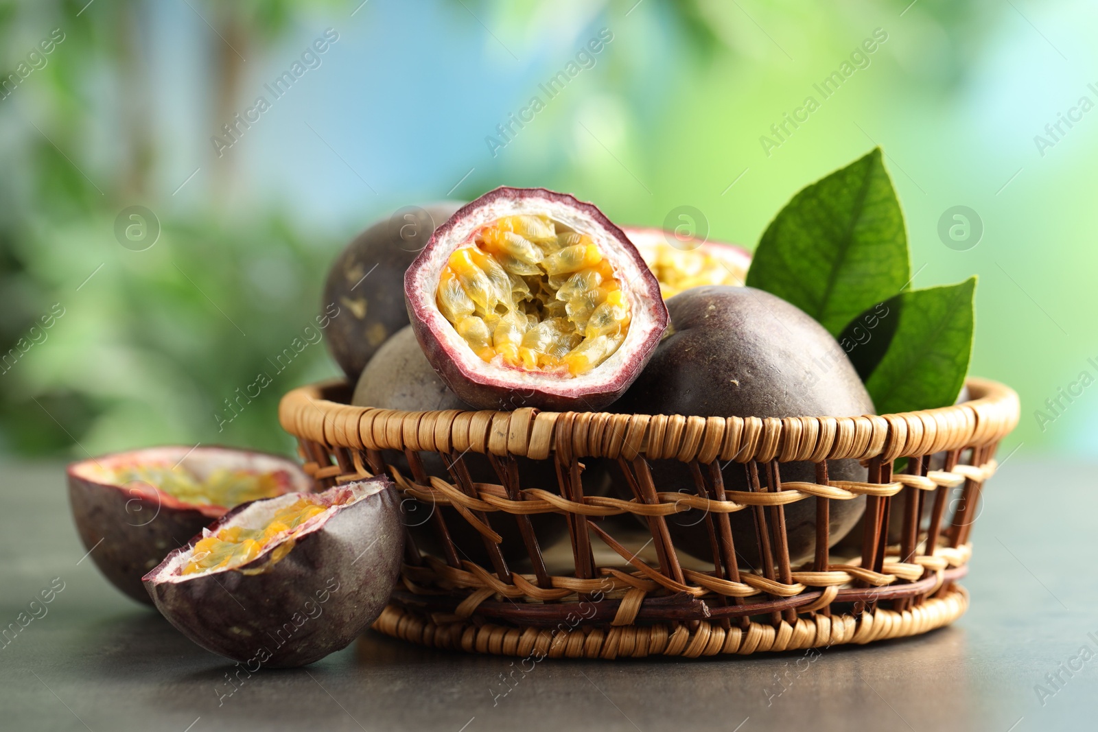 Photo of Fresh passion fruits in wicker basket on grey table outdoors, closeup
