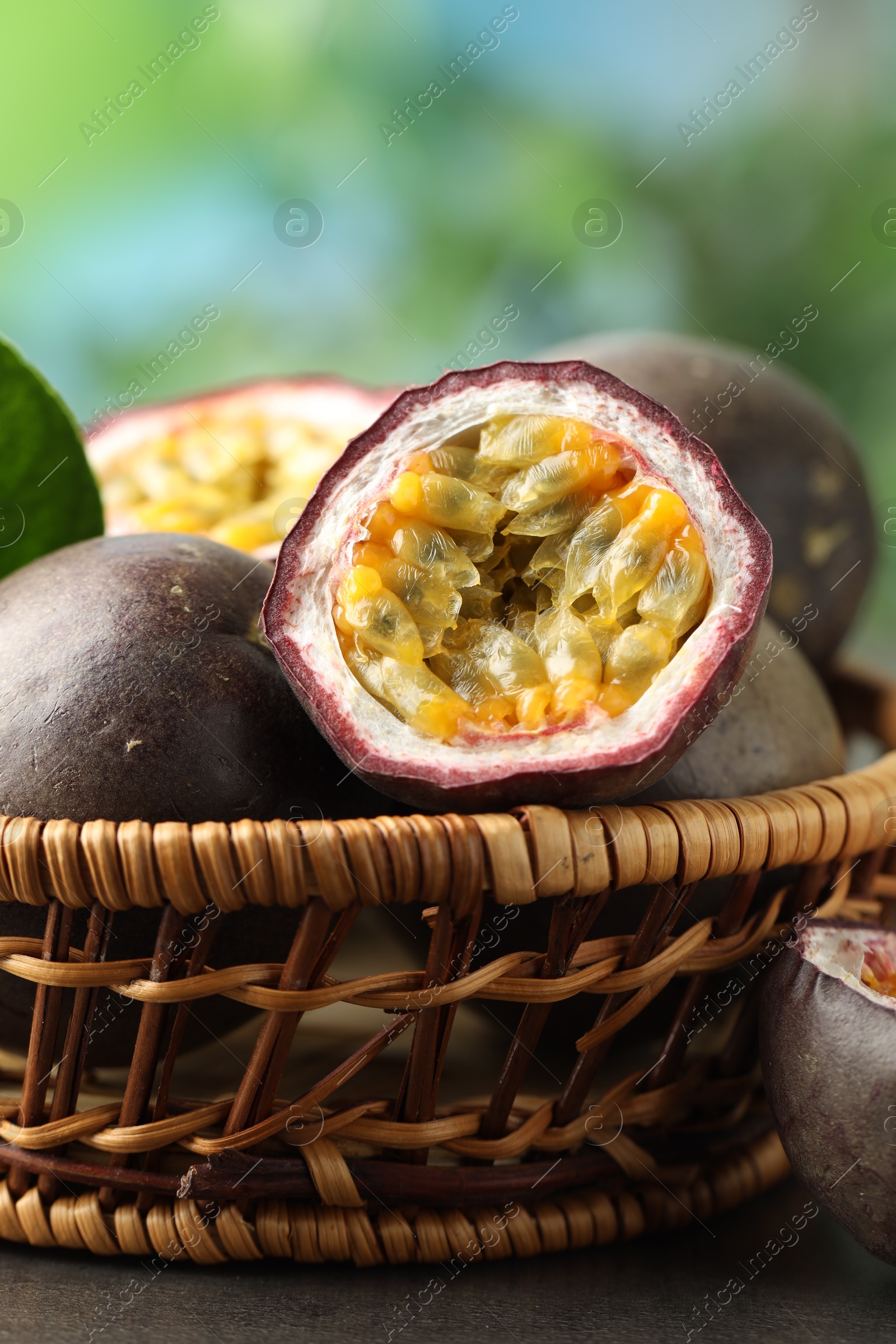 Photo of Fresh passion fruits in wicker basket on grey table outdoors, closeup