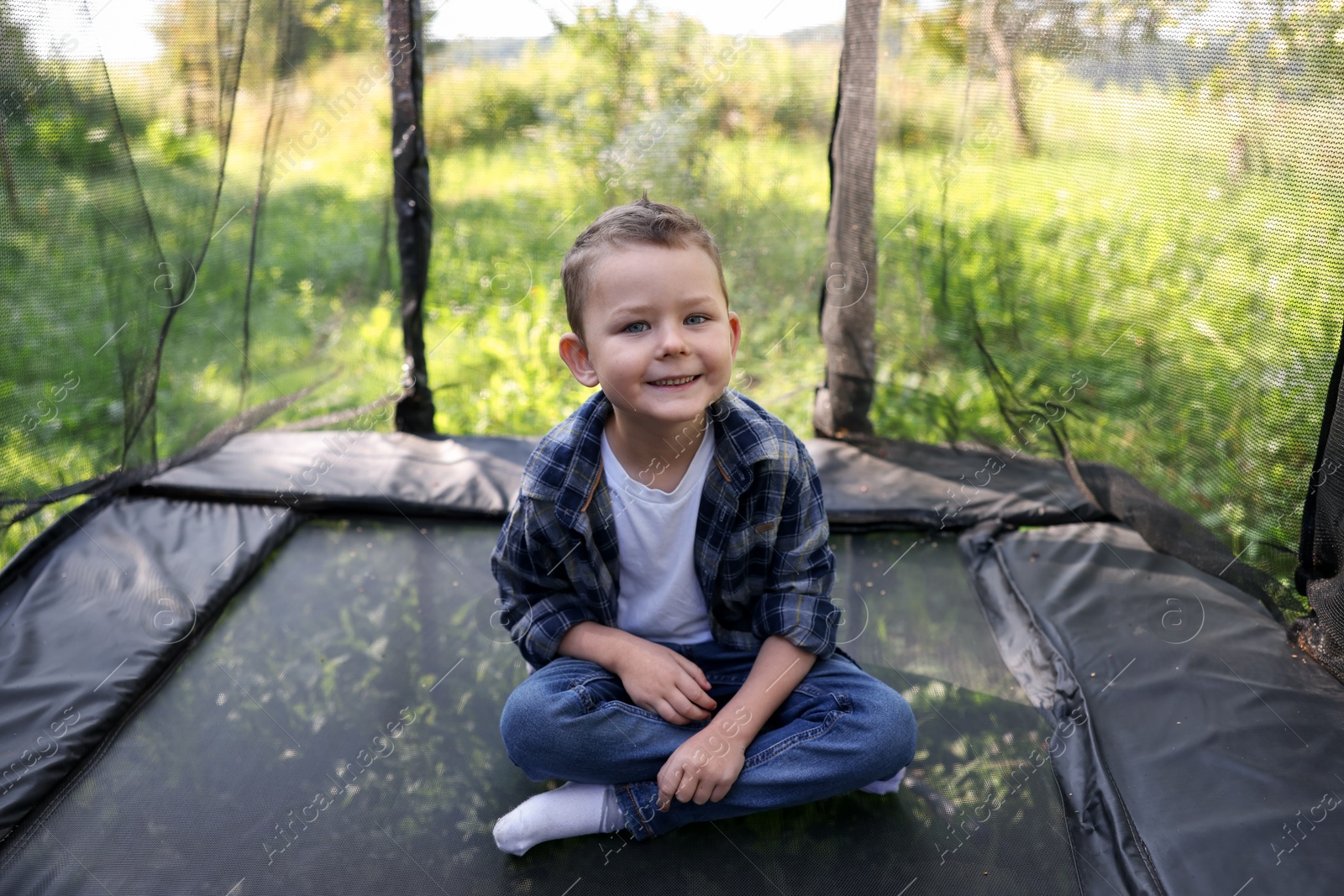 Photo of Happy boy sitting on black trampoline outdoors