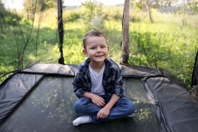 Photo of Happy boy sitting on black trampoline outdoors
