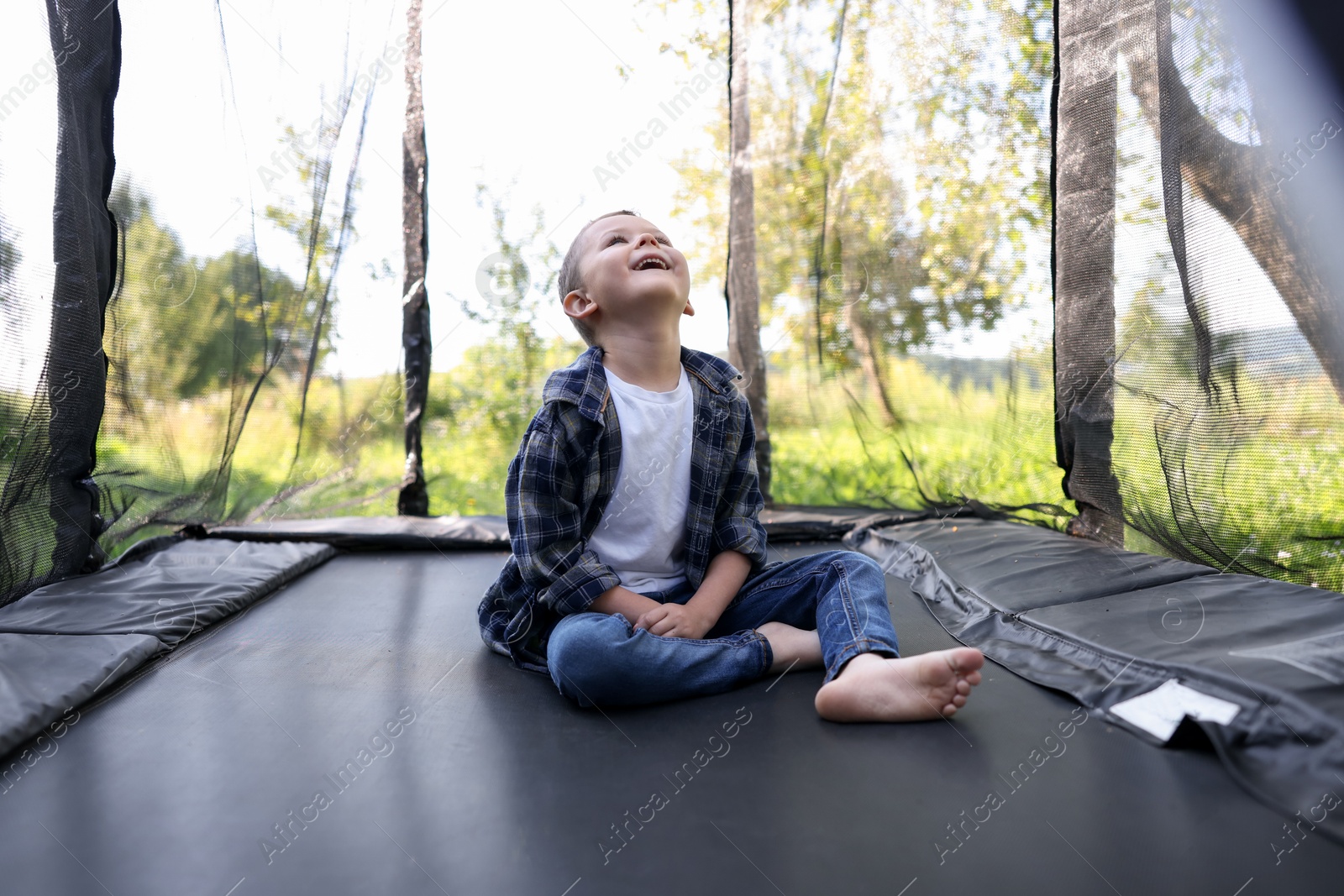 Photo of Happy boy sitting on black trampoline outdoors