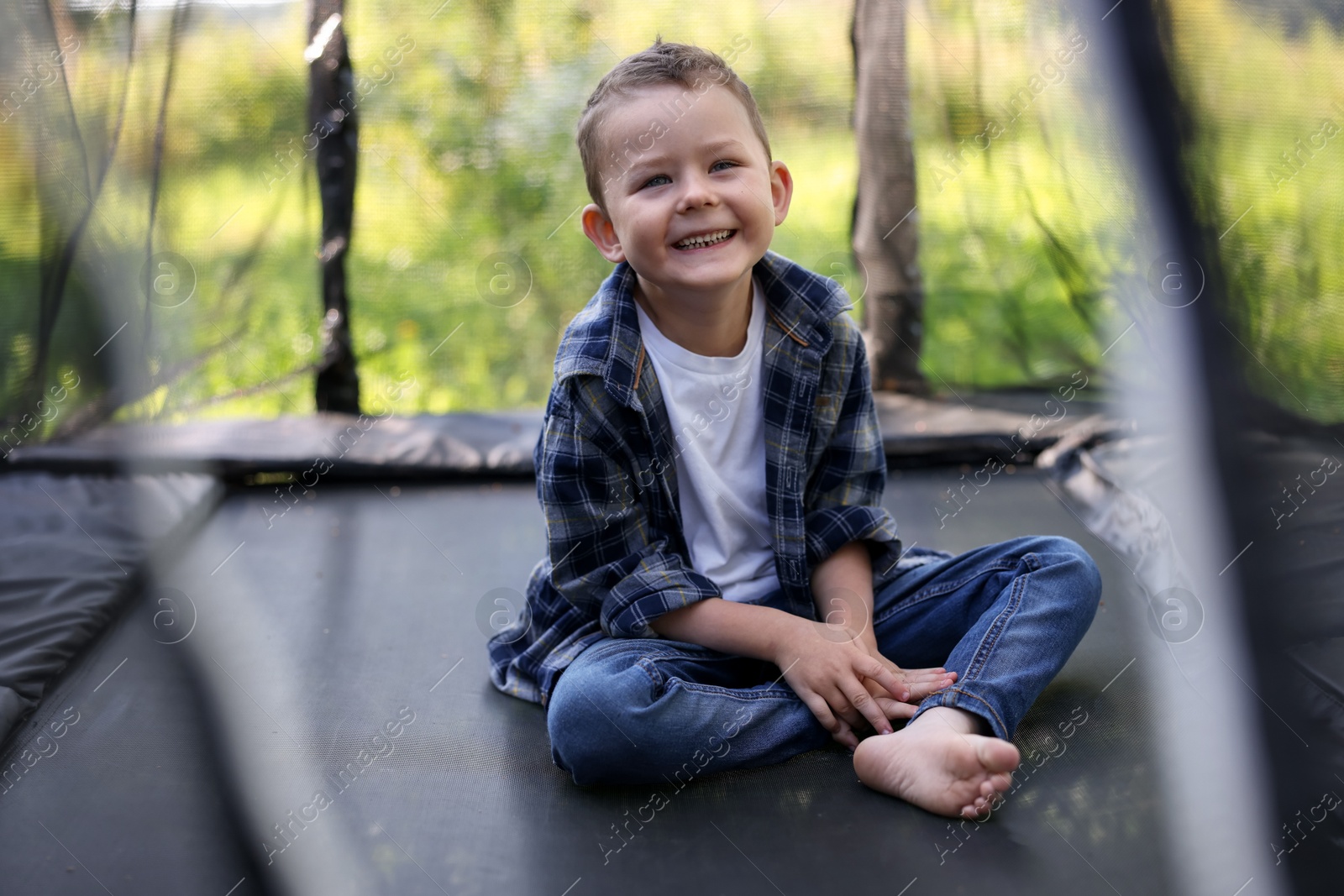 Photo of Happy boy sitting on black trampoline outdoors