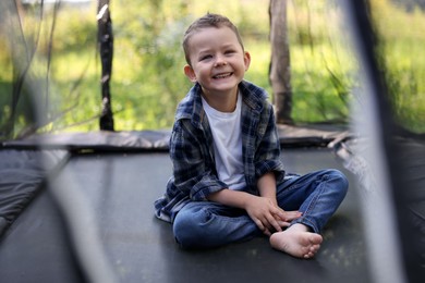 Photo of Happy boy sitting on black trampoline outdoors