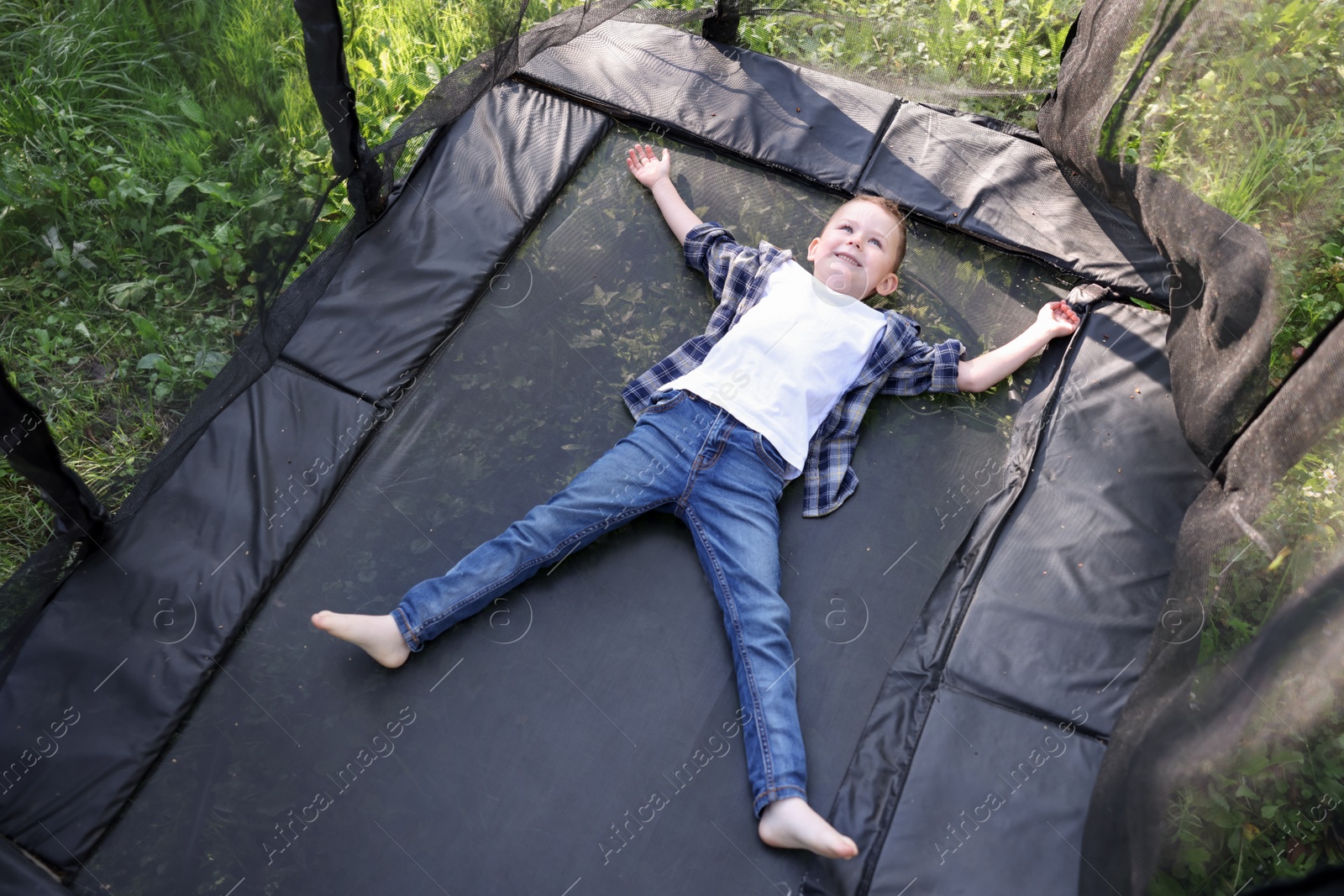 Photo of Happy little boy lying on black trampoline outdoors, above view