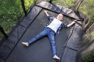 Photo of Happy little boy lying on black trampoline outdoors, above view