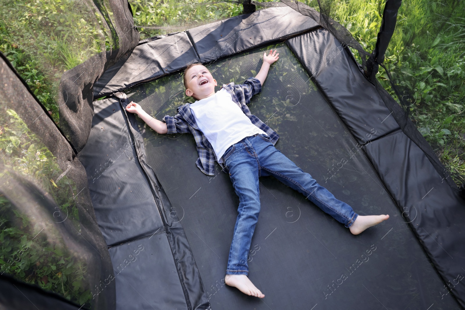 Photo of Happy little boy lying on black trampoline outdoors, above view