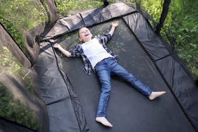 Photo of Happy little boy lying on black trampoline outdoors, above view