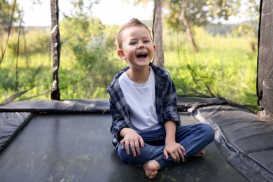 Photo of Happy boy sitting on black trampoline outdoors