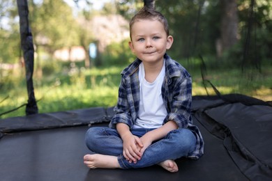 Photo of Cute little boy sitting on black trampoline outdoors