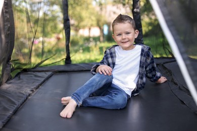 Photo of Happy little boy posing on black trampoline outdoors