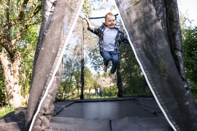 Photo of Cute little boy jumping on black trampoline outdoors